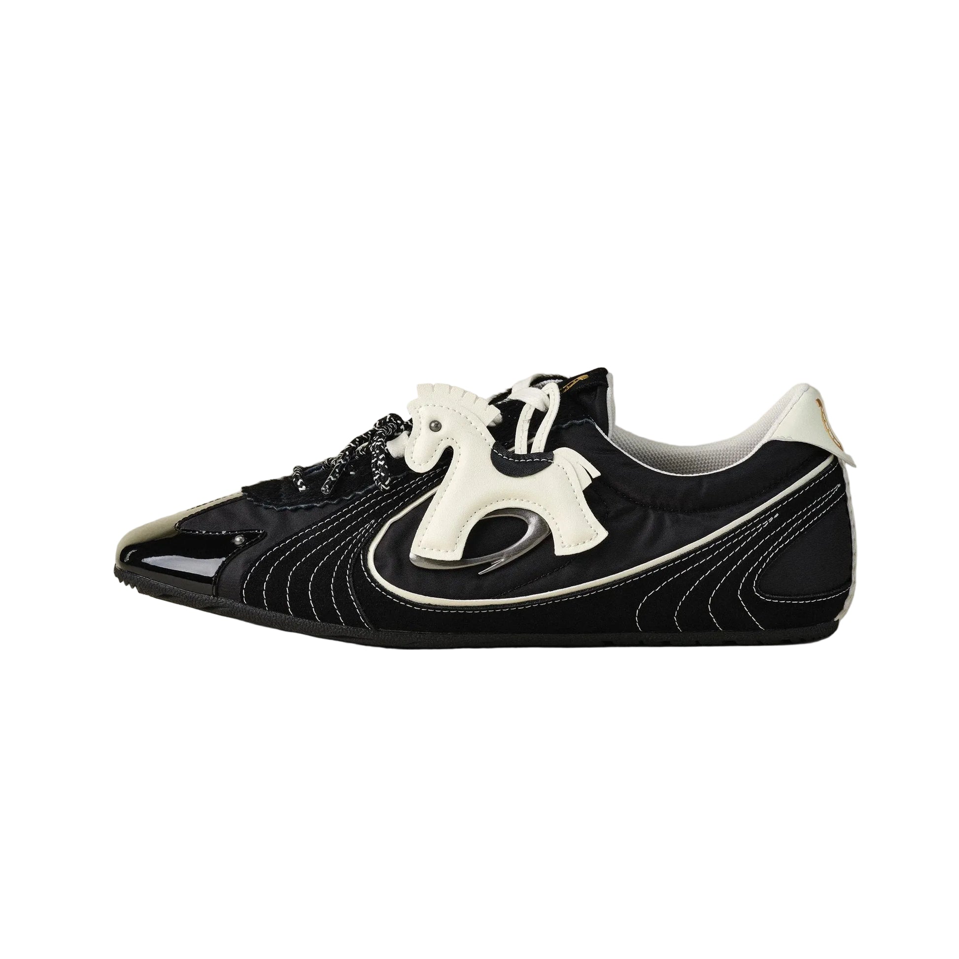 A black leather sneaker with a glossy black toe cap, white sculptural side detail, and white laces, photographed from the side against a neutral light gray background.