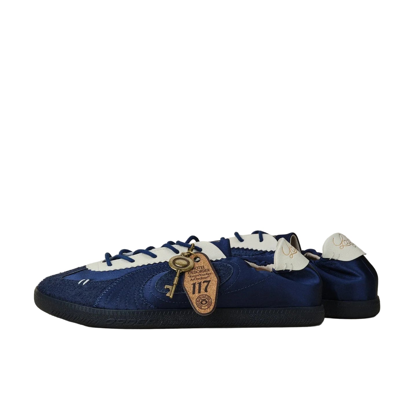 A pair of blue suede and satin low-top sneakers with white laces and a decorative gold key charm, photographed on a neutral beige background.