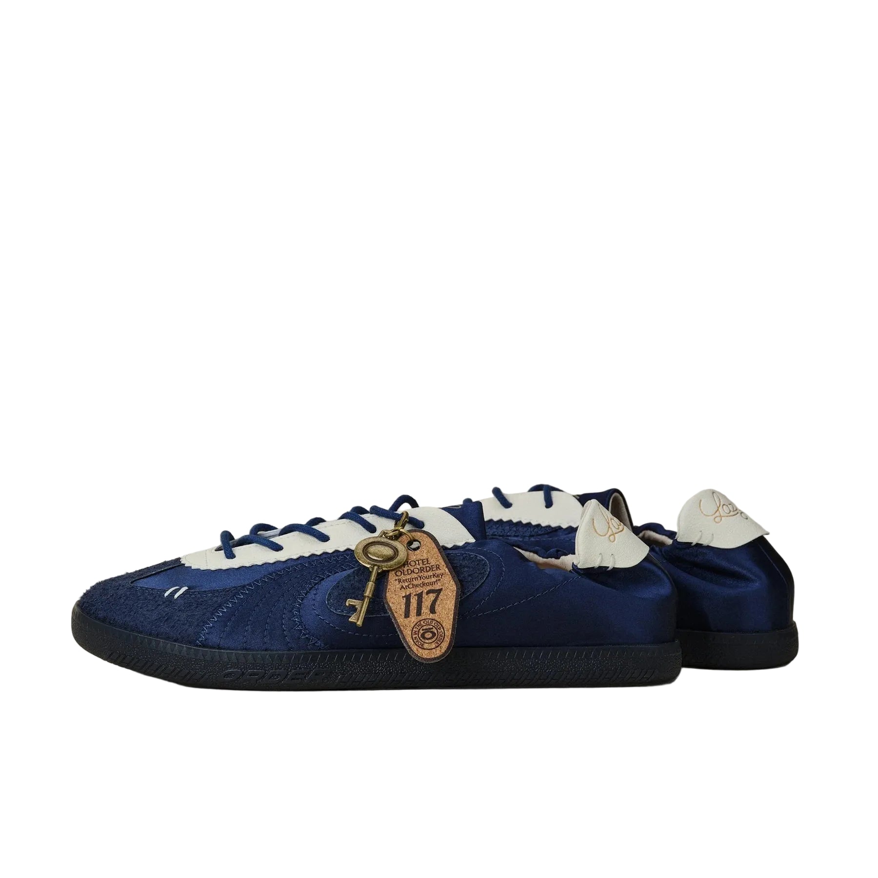A pair of blue suede and satin low-top sneakers with white laces and a decorative gold key charm, photographed on a neutral beige background.