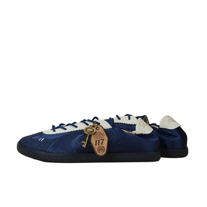 A pair of blue suede and satin low-top sneakers with white laces and a decorative gold key charm, photographed on a neutral beige background.
